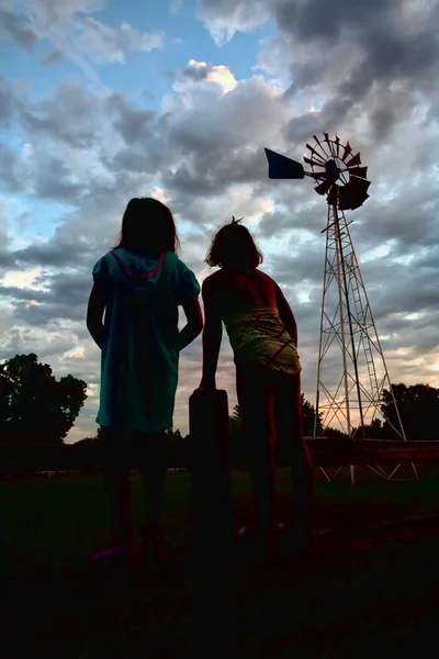 Meninas olham para moinho de vento ao pôr do sol . — Fotografia de Stock