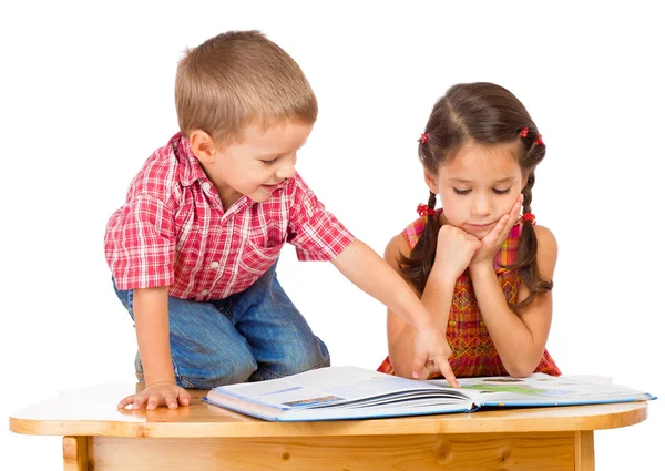 Dos niños sonrientes leyendo un libro en el escritorio —  Fotos de Stock