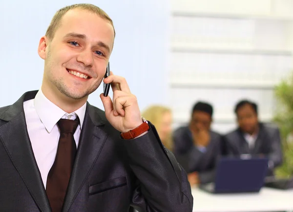 Ο άνθρωπος των επιχειρήσεων μιλώντας στο τηλέφωνο σε ένα γραφείο με την ομάδα του πίσω από — Φωτογραφία Αρχείου