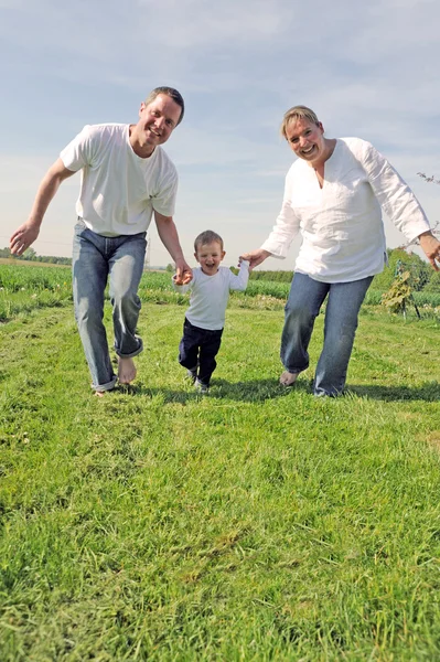 Young family with a toddler running across the field together — Stock Photo, Image