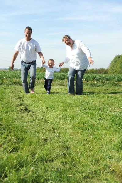 Família jovem com uma criança correndo pelo campo juntos — Fotografia de Stock