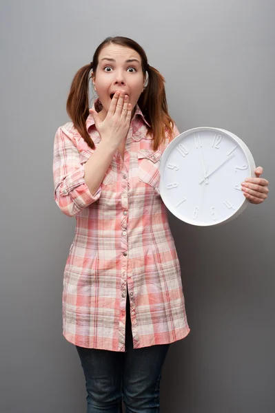 Jeune femme effrayée montrant horloge murale — Photo