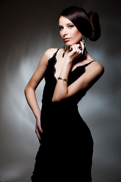 Alluring woman in black dress posing over dark background