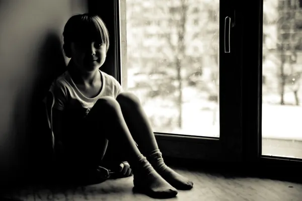 Samotny dziecko siedzi w oknie. — Zdjęcie stockowe