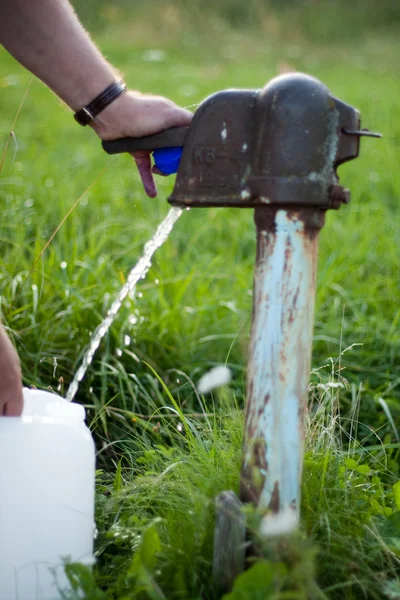 Um homem recolhe a água da velha bomba de água. — Fotografia de Stock