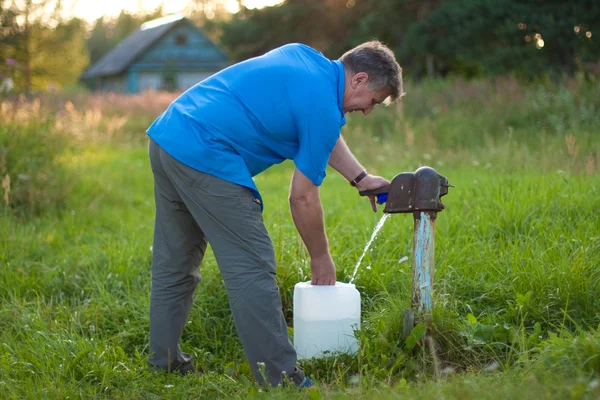 stock image A man collects the water from the old water pump