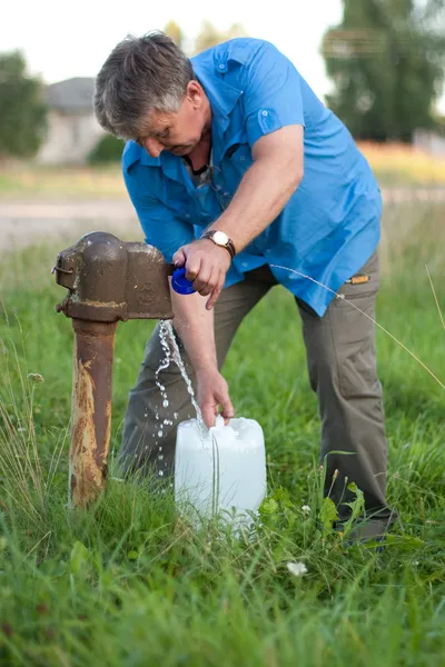 एक माणूस जुन्या पाण्याच्या पंपमधून पाणी गोळा करतो — स्टॉक फोटो, इमेज