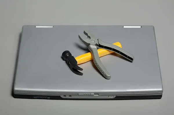 Un portátil roto con un martillo y alicates — Foto de Stock