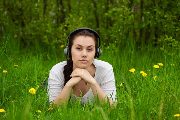 Menina com fones de ouvido deitado na grama ans olhando streight — Fotografia de Stock