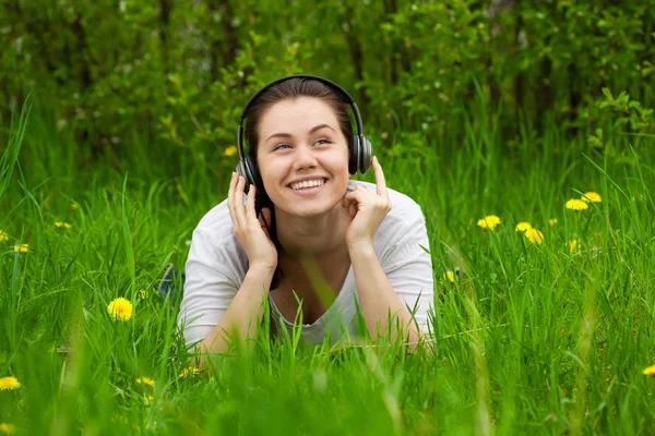 Mulher rindo com fones de ouvido na grama — Fotografia de Stock