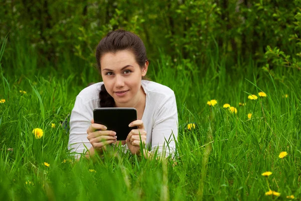 Усміхнена дівчина з електронною книгою лежить на траві — стокове фото