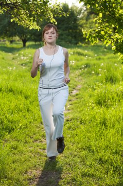 Young woman runing in a park and listen to music clipart