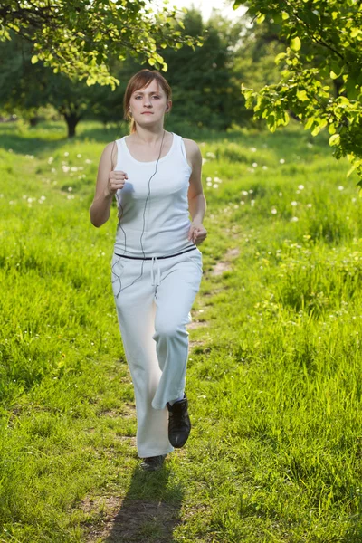 Mujer joven corriendo en un parque y escuchando música Imagen de archivo