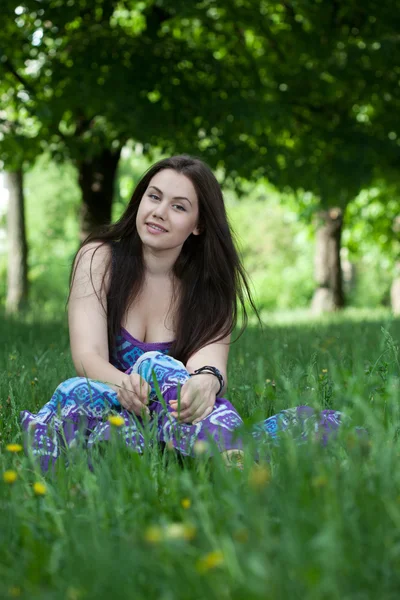 Unga leende kvinna sitter i gräset Royaltyfria Stockfoton