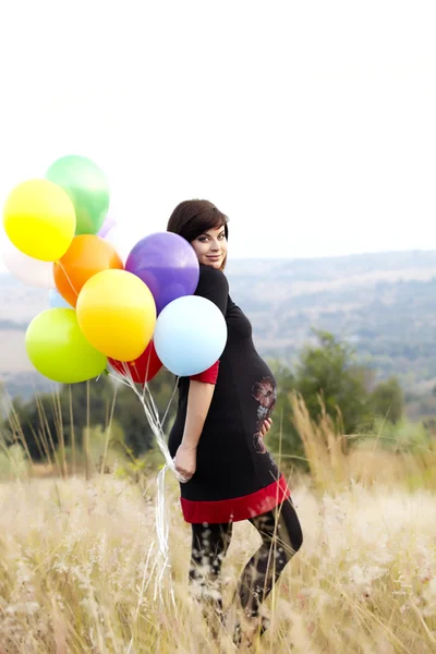 Беременная женщина с воздушными шарами в траве — стоковое фото