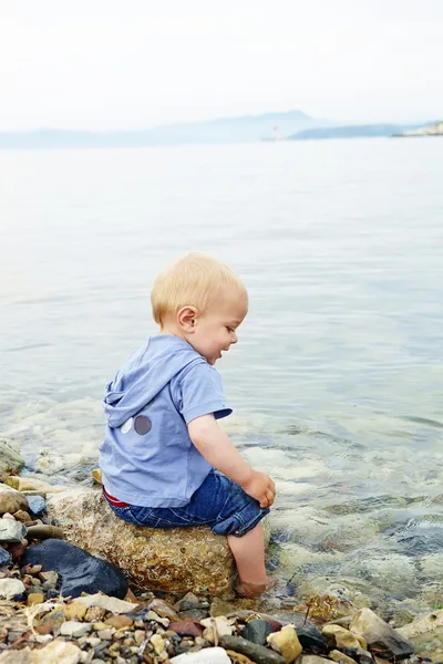 Little blond one year old boy sitting on a rock