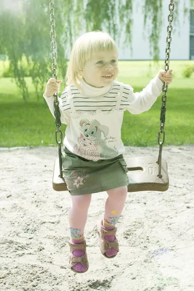 Годовалая девочка катается по парку на качелях — стоковое фото