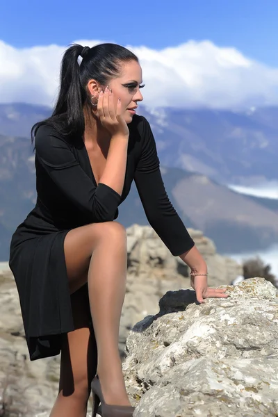 Femme en robe noire assise sur un rocher — Photo