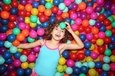 Little girl playing lying in colorful balls park playground clipart