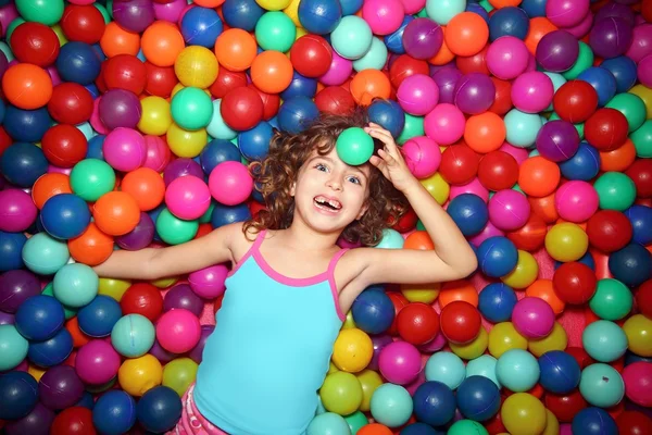 Little girl playing lying in colorful balls park playground — Stock Photo, Image