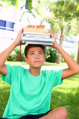 Boy teenager student holding head stacked books