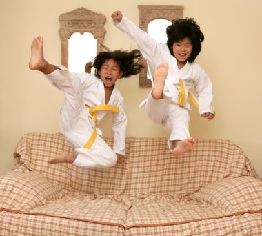 Two little asian judo gils jump on sofa clipart