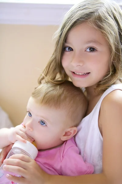 Toddler girl giving bottle of milk to baby sister — Stock Photo, Image