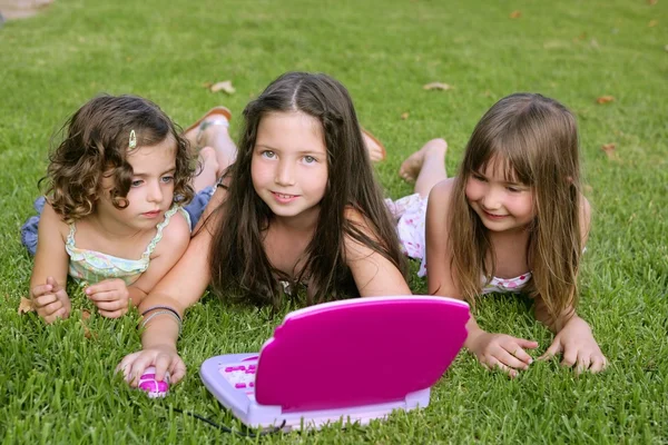 Три дівчинки грають з іграшковим комп'ютером у траві — стокове фото