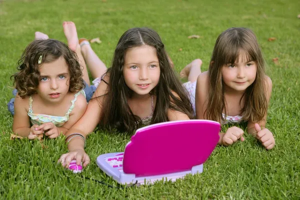 Tre lilla flicka som leker med leksak dator i gräs — Stockfoto