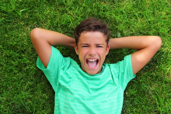 Menino rindo adolescente que estabelece grama verde — Fotografia de Stock