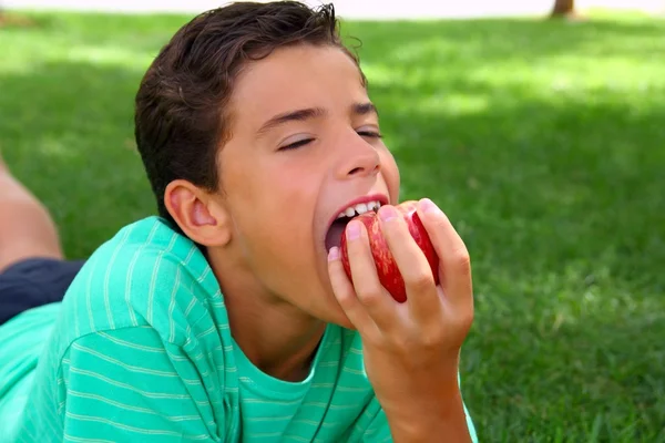 Menino adolescente comendo maçã vermelha na grama do jardim — Fotografia de Stock
