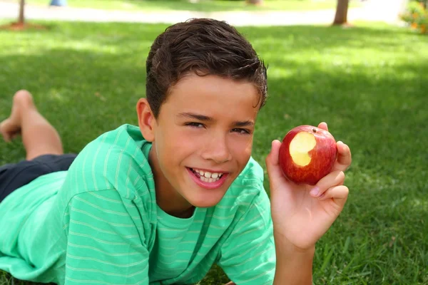 Хлопчик підліток їсть червоне яблуко на садовій траві — стокове фото