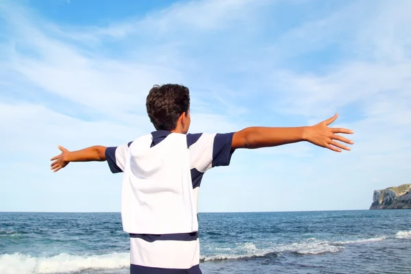 Мальчик-подросток с открытыми руками смотрит на синее море — стоковое фото