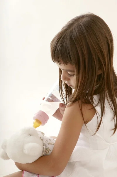 Morena menina alimentando garrafa ursinho de pelúcia — Fotografia de Stock