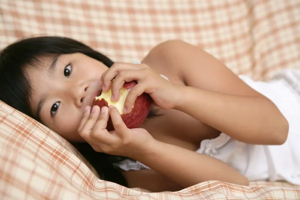 Ασιατικό κορίτσι τρώει κόκκινο μήλο πέρα από τον καναπέ — Φωτογραφία Αρχείου
