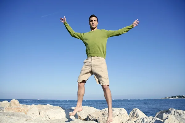 Junger Mann springt in ozeanblauem Ufer über Steine — Stockfoto