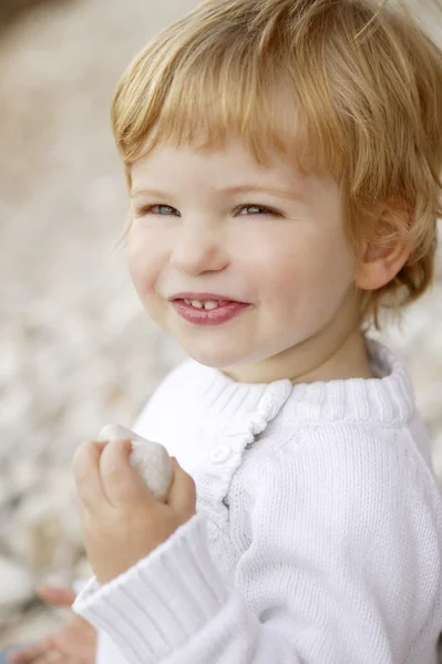 Niño rubio sonriendo sobre un fondo de piedras rodantes — Foto de Stock