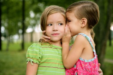 Two twin little sister girls whisper in ear clipart