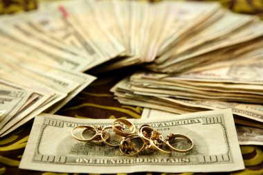 Dollar notes and gold rings over tablecloth clipart