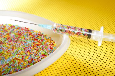 Little colorful candy syringe over yellow background