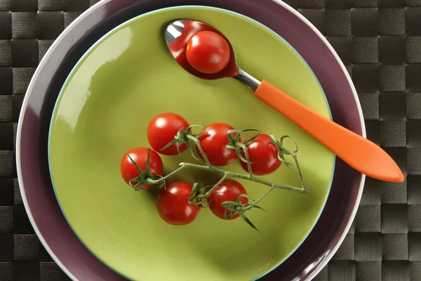 Röda körsbärstomater gren, sked och gröna maträtt — Stockfoto