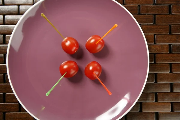 Snack de tomates en un plato morado y palitos de colores —  Fotos de Stock