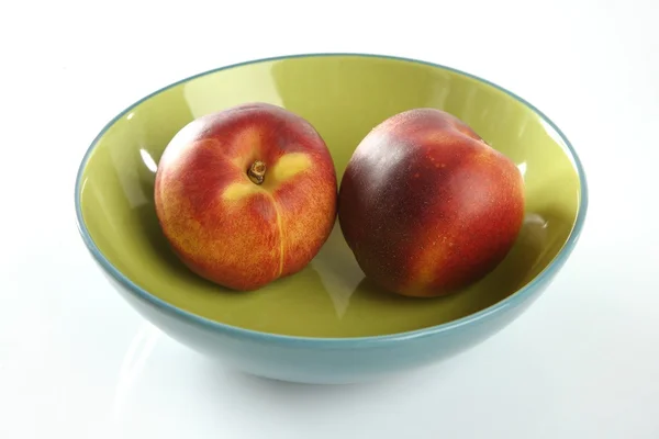 Två röda persikor i en grön skål — Stockfoto
