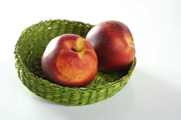 Två röda persikor i en grön korg — Stockfoto