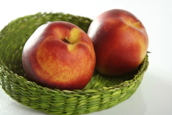 Zwei rote Pfirsiche in einem grünen Korb — Stockfoto