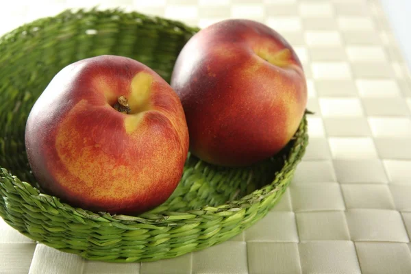 Dois pêssegos vermelhos em uma cesta verde — Fotografia de Stock