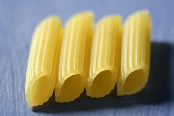 Négy sárga makaróni, egy vonal, makró-kék háttér — Stock Fotó