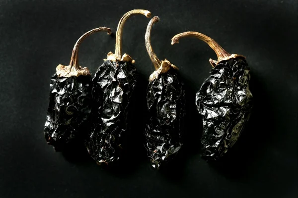 Four Black mexican dried chili peppers black background — Stock Photo, Image