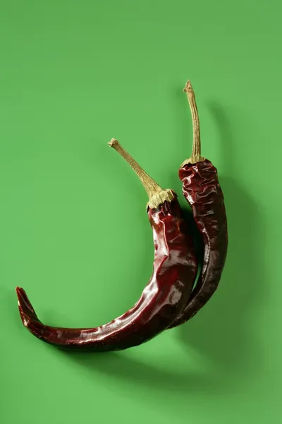 Dvě sušené papriky, chilli, přes zelené pozadí — Stock fotografie
