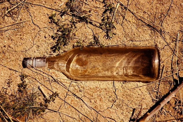 Стеклянная прозрачная бутылка на глиняном полу — стоковое фото